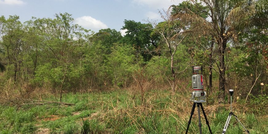 Two measuring devices stand on tripods in green, wooded surroundings.